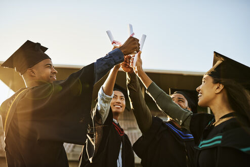 Gruppe fröhlicher Absolventen, die gemeinsam Diplome oder Zertifikate hochhalten und feiern