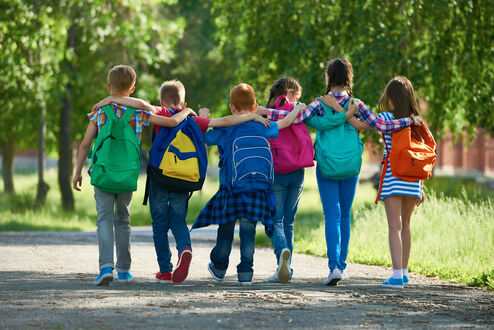 Gruppe von Klassenkameraden mit Schultaschen, die sich umarmen und gehen